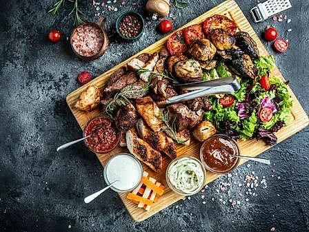 tabla de cortar con varios alimentos hechos a la barbacoa, carnes y verduras